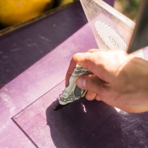 A hand placing a dollar into a donation box outdoors, symbolizing generosity and charity.